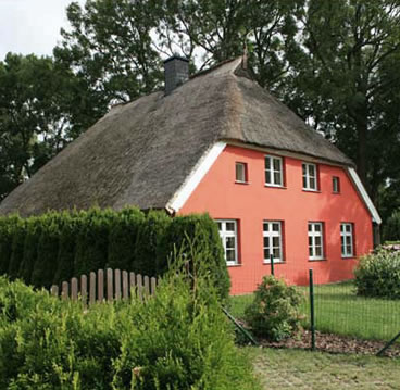 Projekt aus der Entwurf-Galerie von Falk Architekturbüro: Haus mit Reetdach und roter Fassade hinter einer Hecke